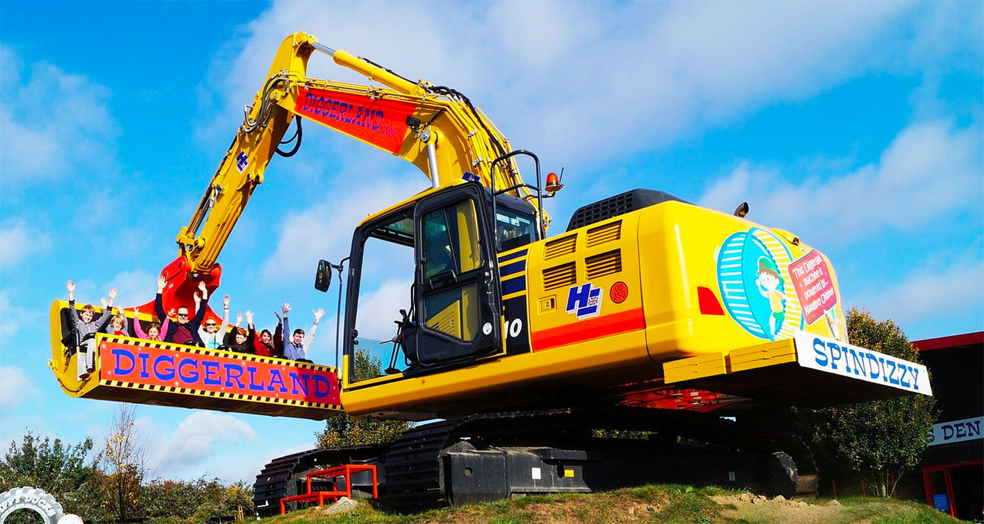 Image of large digger with several people sitting in the huge bucket and waving